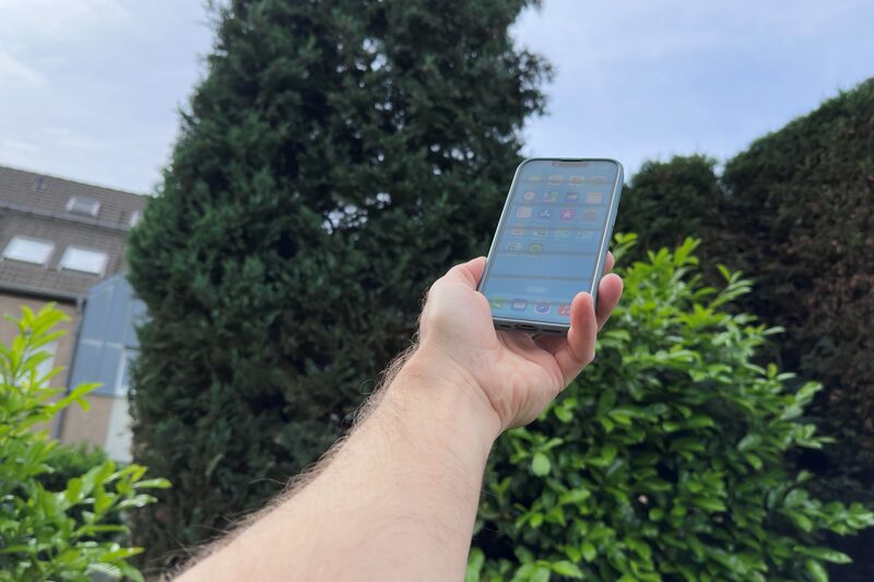 Man sieht einen Arm, der ein Handy in einem Garten in die Luft hält.